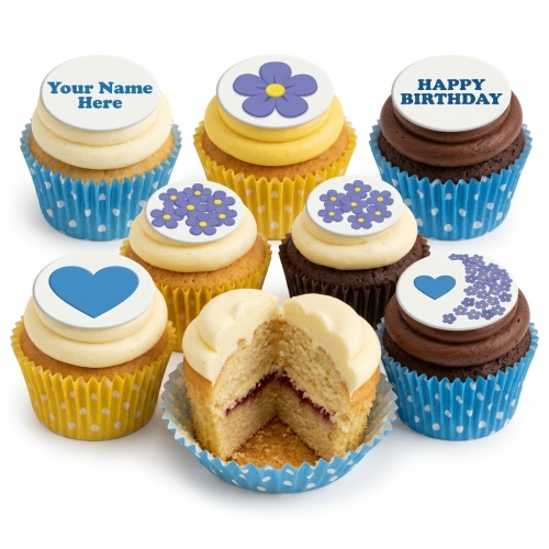 A selection of cupcakes with white frosting and edible toppers featuring purple flowers, blue hearts, and example text 'Your Name Here' and 'Happy Birthday'.