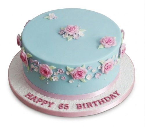 Light blue round cake decorated with pink sugar roses, green leaves, and small white flowers.