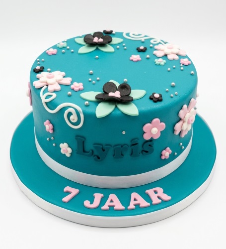 Round teal birthday cake with pink, mint, and black fondant flowers, white swirls, and silver sprinkles, with space for custom name and age.