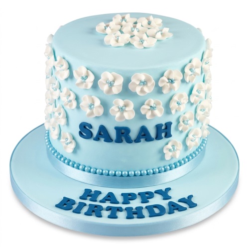 Elegant light blue round birthday cake with white sugar flowers and blue pearl decorations, with a custom name and 'Happy Birthday' message.