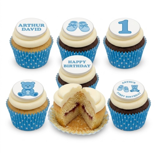 Assortment of blue and white first birthday cupcakes with teddy bears, booties, and custom age '1' toppers.