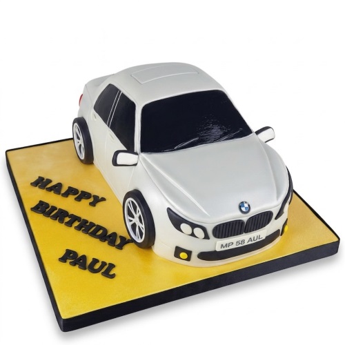 White 3D BMW car shaped birthday cake on a yellow board with "Happy Birthday" message.