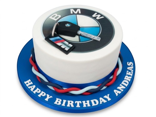 Round white BMW themed birthday cake with edible logo and 3D car key decoration on a blue board.