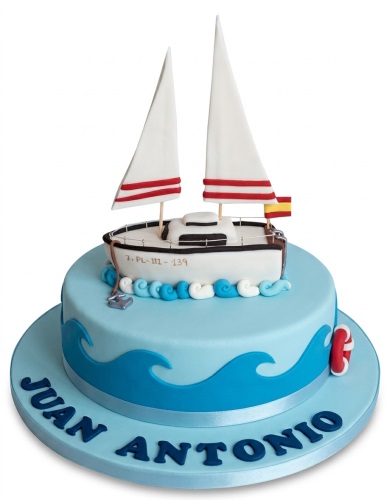 Two-tier blue sailing boat birthday cake with white sails, red stripes, and custom name.