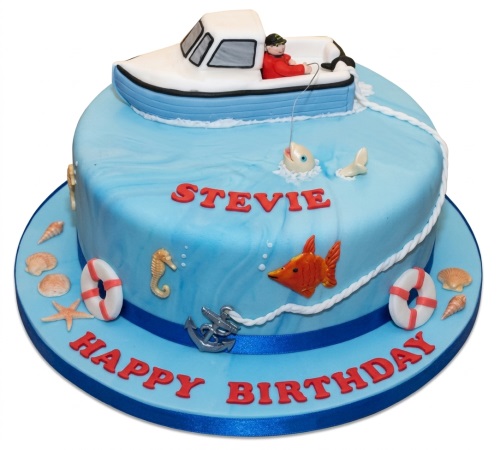 Round blue fishing boat birthday cake with fisherman, fish, seahorse, and seashells.