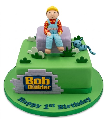 Square green Bob the Builder birthday cake with Bob figurine, Pilchard cat, and "Happy 1st Birthday" message.