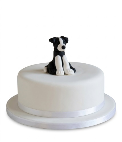 White round birthday cake with a black and white dog figurine topper.
