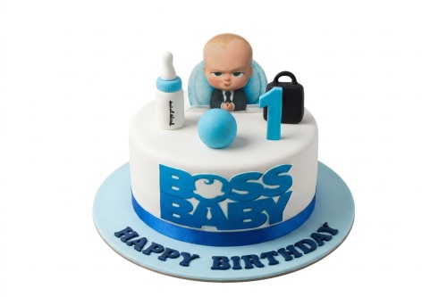 White round Boss Baby 1st birthday cake with blue decorations, baby bottle, briefcase, and number one topper.