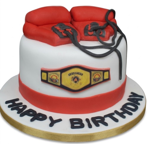 White birthday cake topped with red boxing gloves and a golden championship belt.