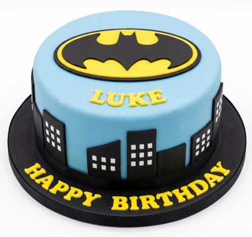 Round blue Batman birthday cake with yellow Bat-Signal and black city skyline decorations.