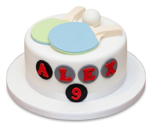 White round cake with edible table tennis rackets, ball, and custom name and age plaques.