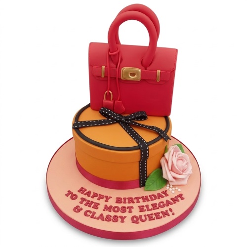 Two-tier birthday cake with a red handbag topper, orange gift box, black ribbon, and pink rose.