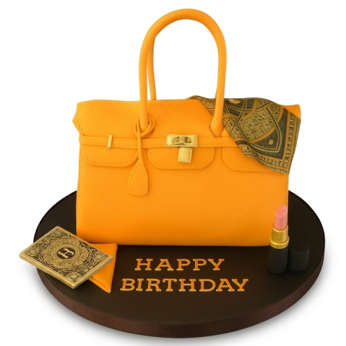 3D orange handbag birthday cake with gold clasp, patterned scarf, decorative initial card, and pink lipstick on a dark board.