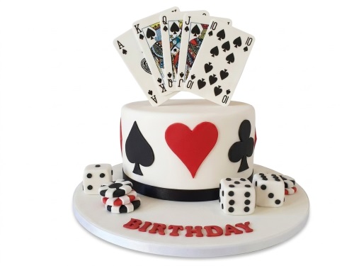 White round birthday cake with edible playing cards, dice, poker chips, and card suit decorations.