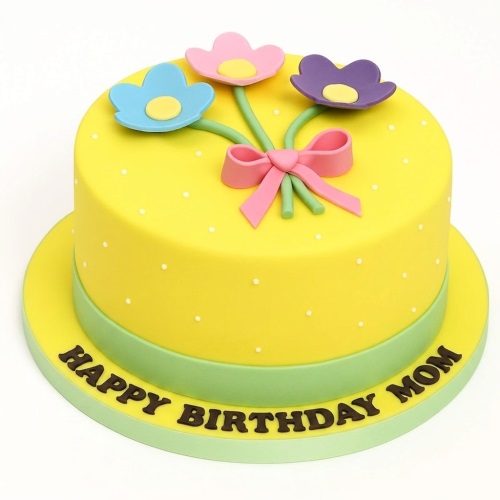 Round yellow birthday cake with white polka dots, green base, and a bouquet of pink, blue, purple fondant flowers tied with a pink bow, with space for a custom message.