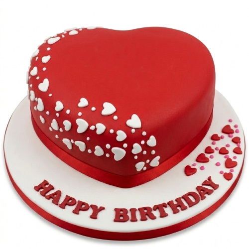 Red heart-shaped birthday cake with white and pink heart decorations on a white board with "Happy Birthday" message.