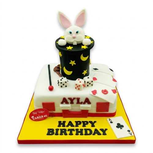 Two-tier magic show birthday cake with rabbit in hat, playing cards, dice, and custom name.