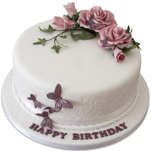 White round birthday cake with pink roses, green leaves, and purple butterflies.