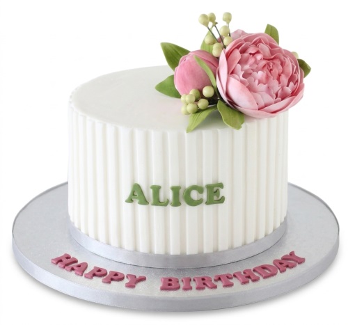 White ribbed birthday cake with pink sugar flowers, green foliage, and a custom name.