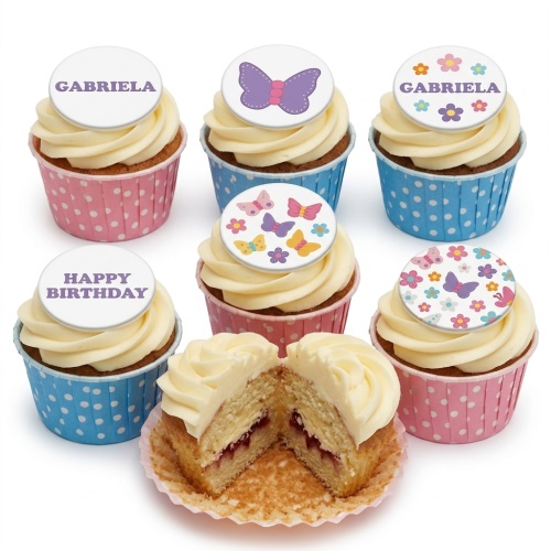 Set of butterfly and floral themed birthday cupcakes with white frosting and pink and blue polka dot wrappers, some with custom name and 'Happy Birthday' toppers.