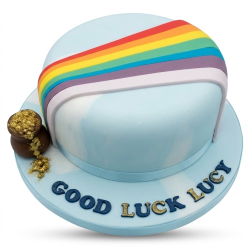 Light blue round cake with a colourful rainbow arch and a brown pot spilling gold glitter, with a custom message on the base.