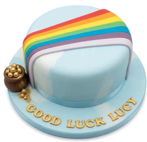 Round light blue cake with a rainbow arch and a pot of gold, with a custom message on the board.