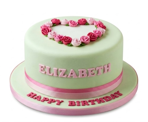 Round pastel green birthday cake with pink sugar roses in a heart shape and pink ribbon.