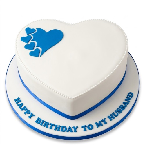 White heart-shaped birthday cake with blue hearts and a blue ribbon, featuring a custom message.