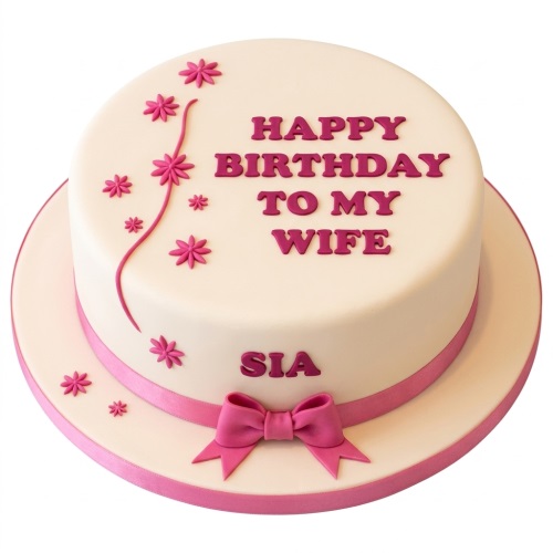 Round white birthday cake with pink fondant flowers, ribbon, and a bow.