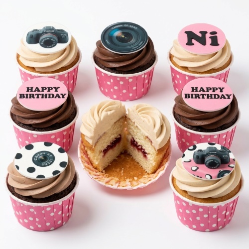 Assortment of photography theme birthday cupcakes with camera and lens toppers in pink wrappers.