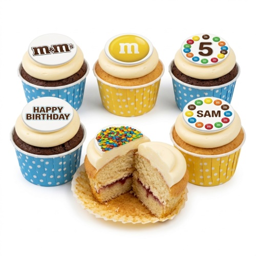 A set of M&M's themed birthday cupcakes with white frosting, some with chocolate sponge and others vanilla, in blue and yellow polka dot cases. Toppers include M&M's logos, mini M&M's, and examples of custom age and personalised messages.