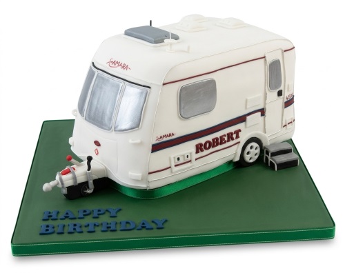 White caravan shaped birthday cake on a green board with a custom 'Happy Birthday' message.