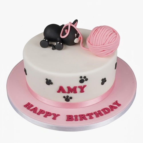 White round birthday cake with a black cat, pink yarn ball, and paw prints.