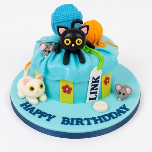 Light blue birthday cake with black and white fondant cats, grey mice, and colourful yarn balls.