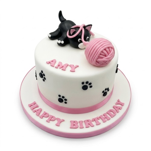 White round birthday cake with a black cat, pink yarn, paw prints, and pink ribbon.
