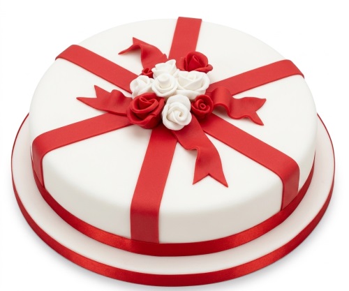 Round white cake with red fondant ribbons, a red bow, and red and white roses on top.
