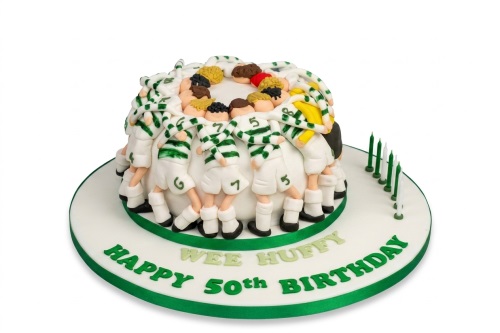 Round white birthday cake with edible football players in a huddle wearing green and white striped jerseys, green and white candles on the side.