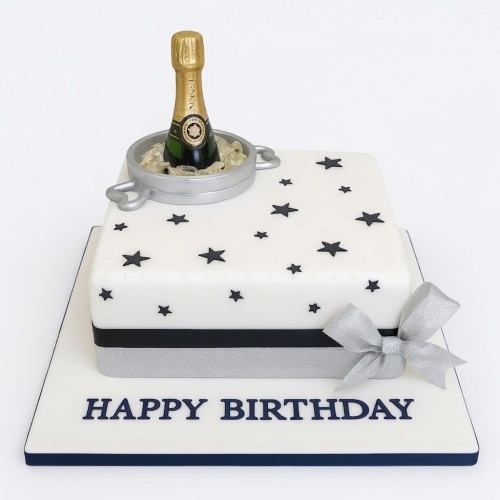 White square birthday cake with black stars, silver ribbon, and a miniature champagne bottle in an ice bucket.