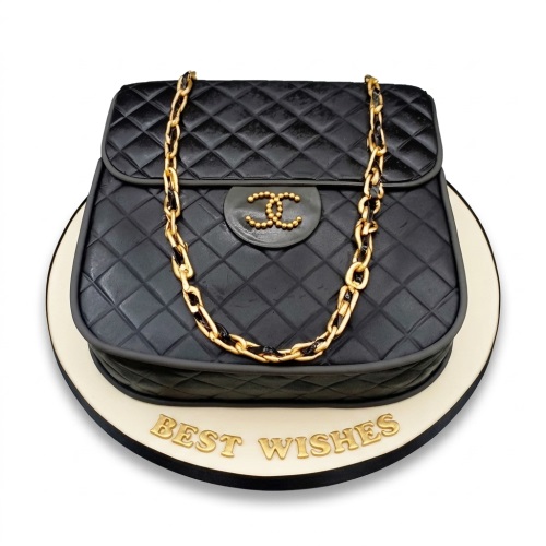 Black quilted handbag cake with gold chain and CC logo on a white board with 'Best Wishes' message.