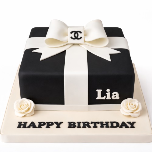 Black and white gift box cake with a white bow, Chanel logo, and white roses, with "Happy Birthday" message.