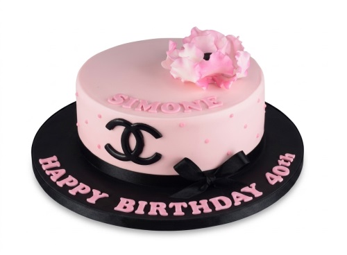 Pink round cake with black Chanel logo, pink sugar flower, black ribbon, and pink polka dots.