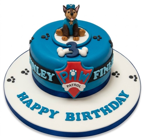 Blue Paw Patrol themed birthday cake with a Chase character figure, Paw Patrol shield, bone decorations, paw prints, and a custom age topper.