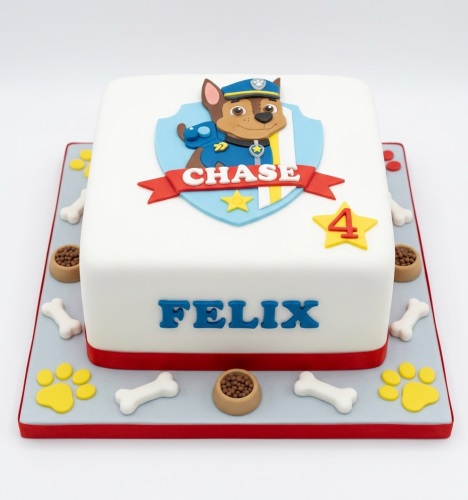 White square Paw Patrol Chase birthday cake with custom name and age topper, decorated with paw prints and bones.