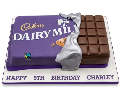 Rectangular cake designed as a Cadbury Dairy Milk chocolate bar with purple wrapper, silver foil, and visible chocolate squares on a white board with a custom message.