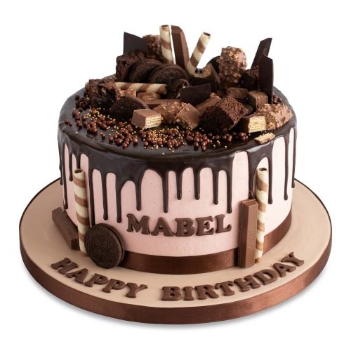 Round chocolate drip birthday cake with chocolate bars, cookies, brownies, and sprinkles on top, with a personalised name and 'Happy Birthday' message.