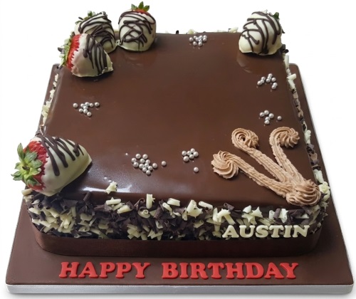 Square chocolate cake with glossy glaze, white and dark chocolate shavings, and white chocolate-dipped strawberries.