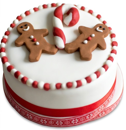 Round white Christmas cake with two gingerbread men, a candy cane, and red and white bead border.