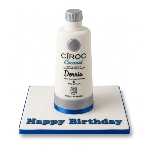 3D Ciroc Coconut bottle-shaped birthday cake with white, silver, and blue details on a white board with a custom 'Happy Birthday' message.