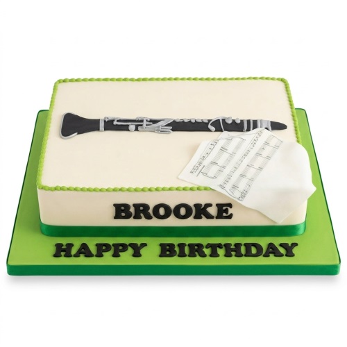 Rectangular cream cake with a black clarinet, sheet music, and green trim on a green board.