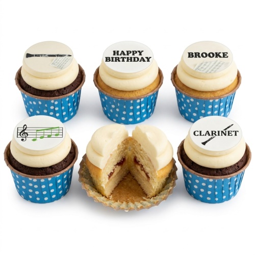 Six cupcakes with white frosting, blue polka dot wrappers, and edible music-themed toppers including clarinets and musical notes. One cupcake is cut open revealing vanilla sponge with jam.